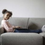 Young girl with laptop on couch.