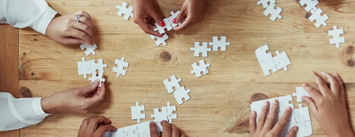 Several pairs of hands putting together blank, white puzzle pieces