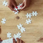 Several pairs of hands putting together blank, white puzzle pieces