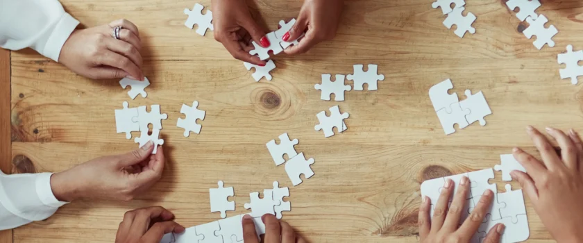 Several pairs of hands putting together blank, white puzzle pieces