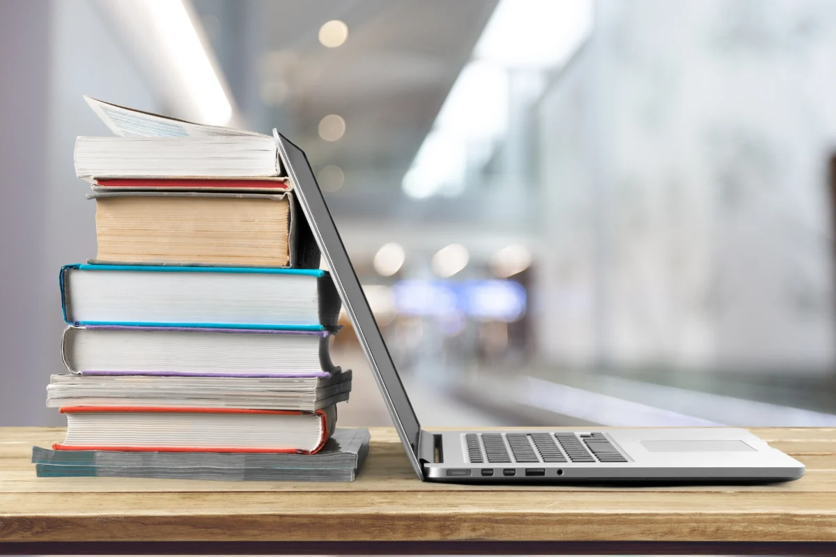 A desk with a laptop and a stack of books on it