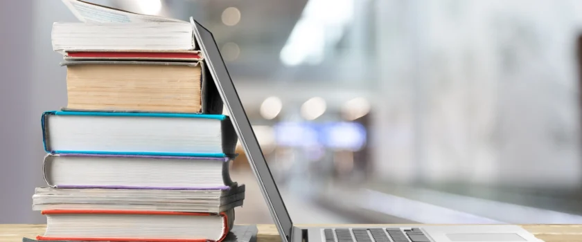 A desk with a laptop and a stack of books on it