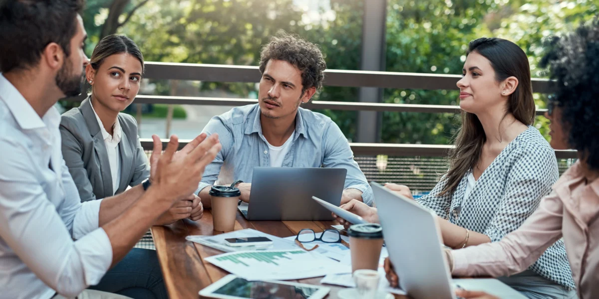 A group of adults sitting around a table outdoors, having a discussion